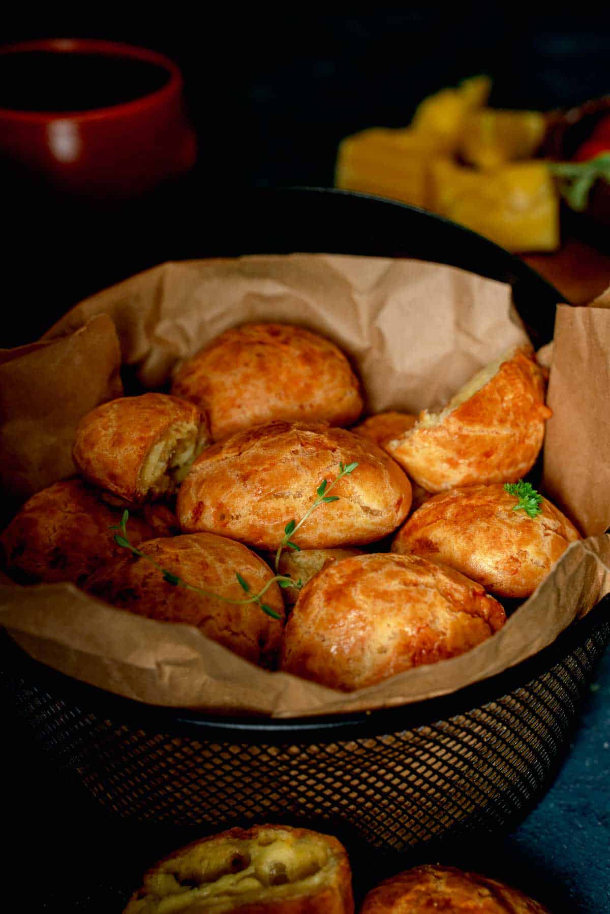 A rich and dark photo showing off a basket of french cheese puffs wrapped in paper.