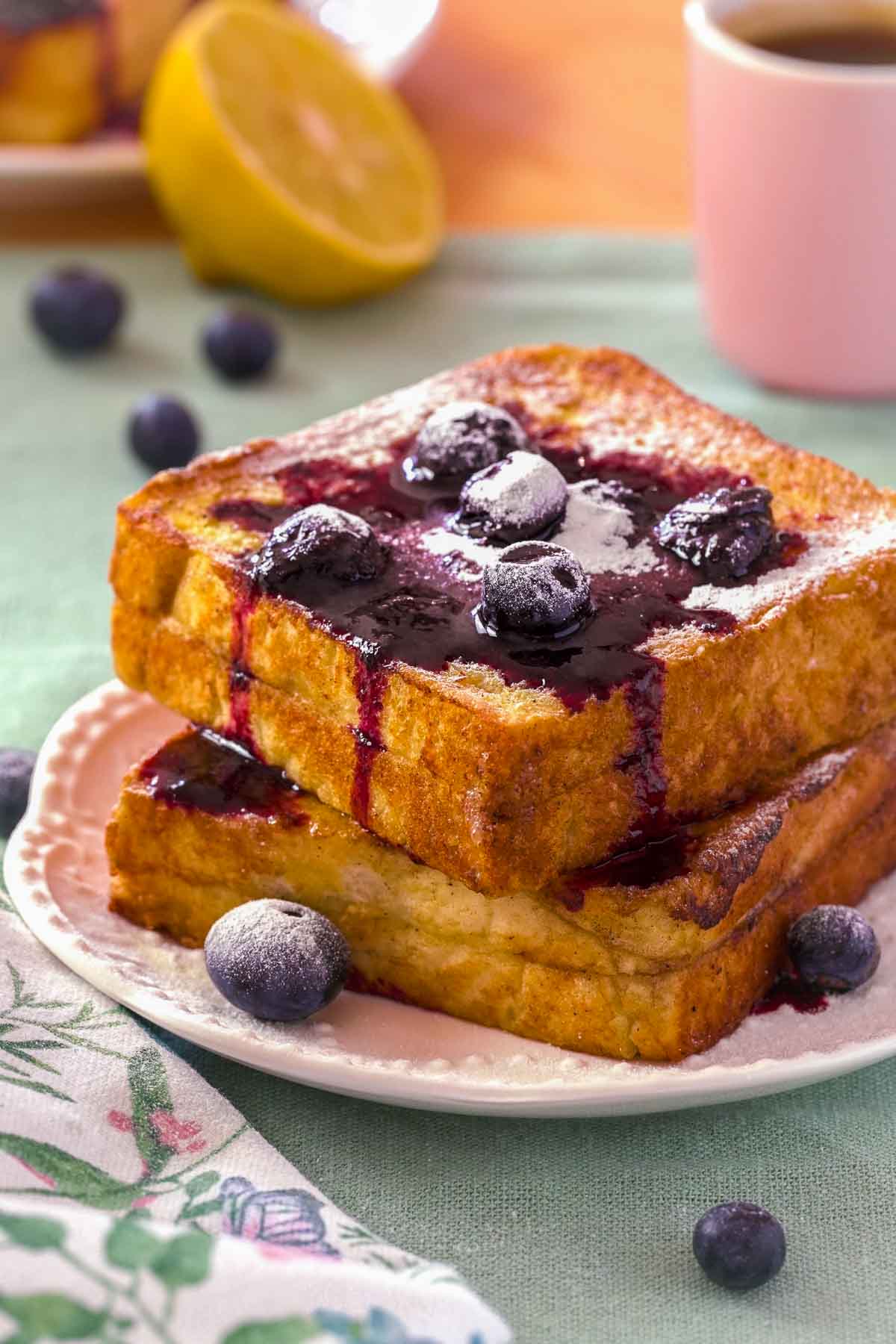 Lemon Blueberry French Toast on a white plate. The stuffed French toast is topped with blueberry compote, fresh blueberries, and icing sugar.