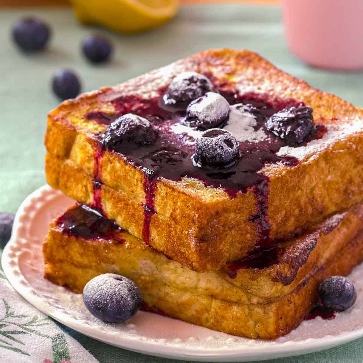 A stack of lemon blueberry french toast on a white plate. The toast is topped with blueberry compote