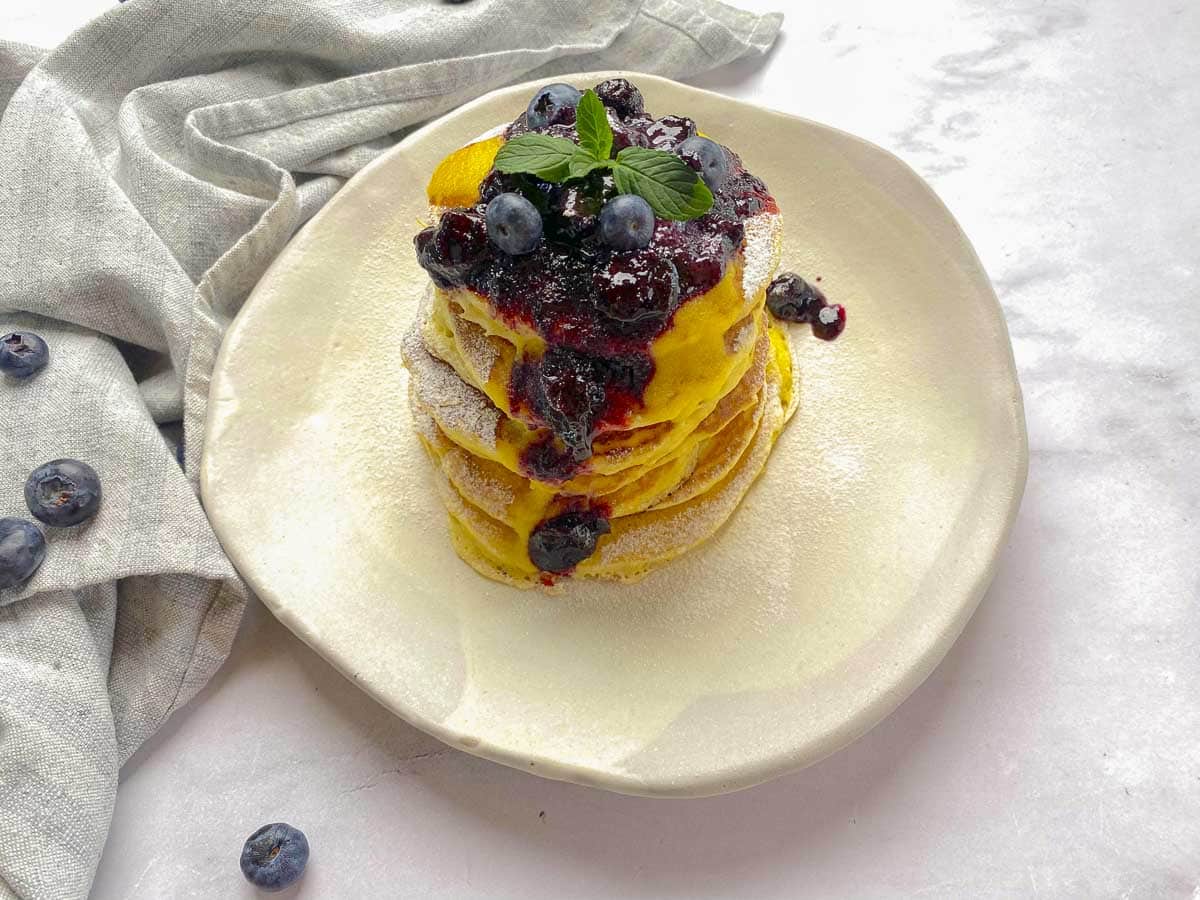 A high stack of fluffy lemon ricotta pancakes on a white plate.