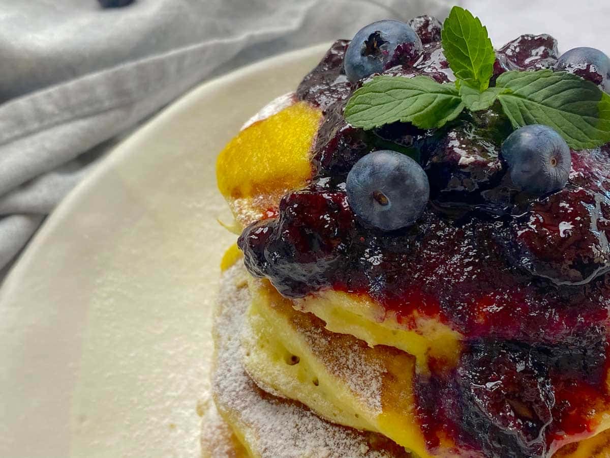 A close-up of blueberry compote on top of some fluffy pancakes.