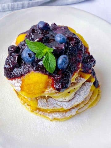 A stack of lemon ricotta pancakes covering in a blueberry compote on a white plate.