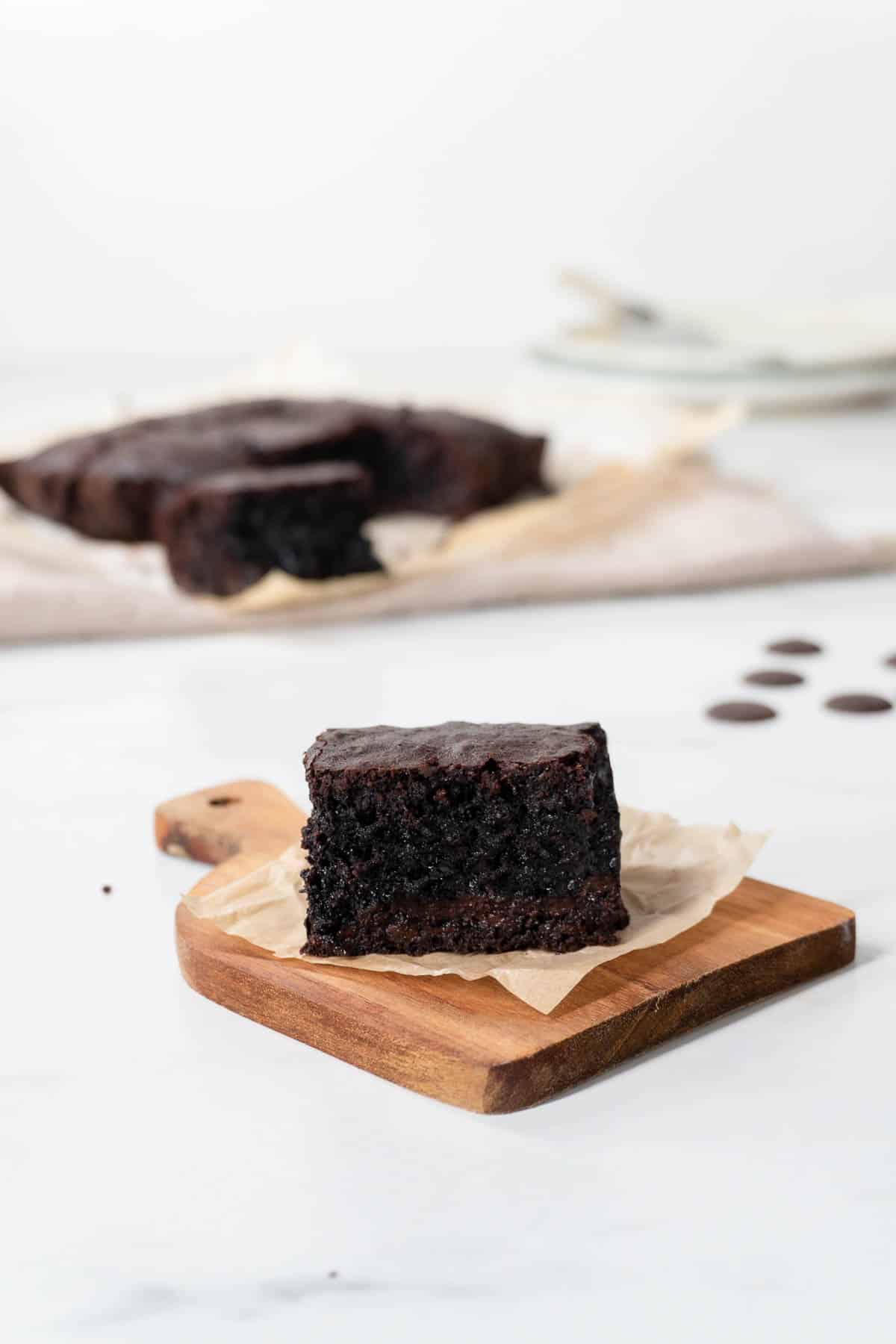A single olive oil brownie on a wooden board.