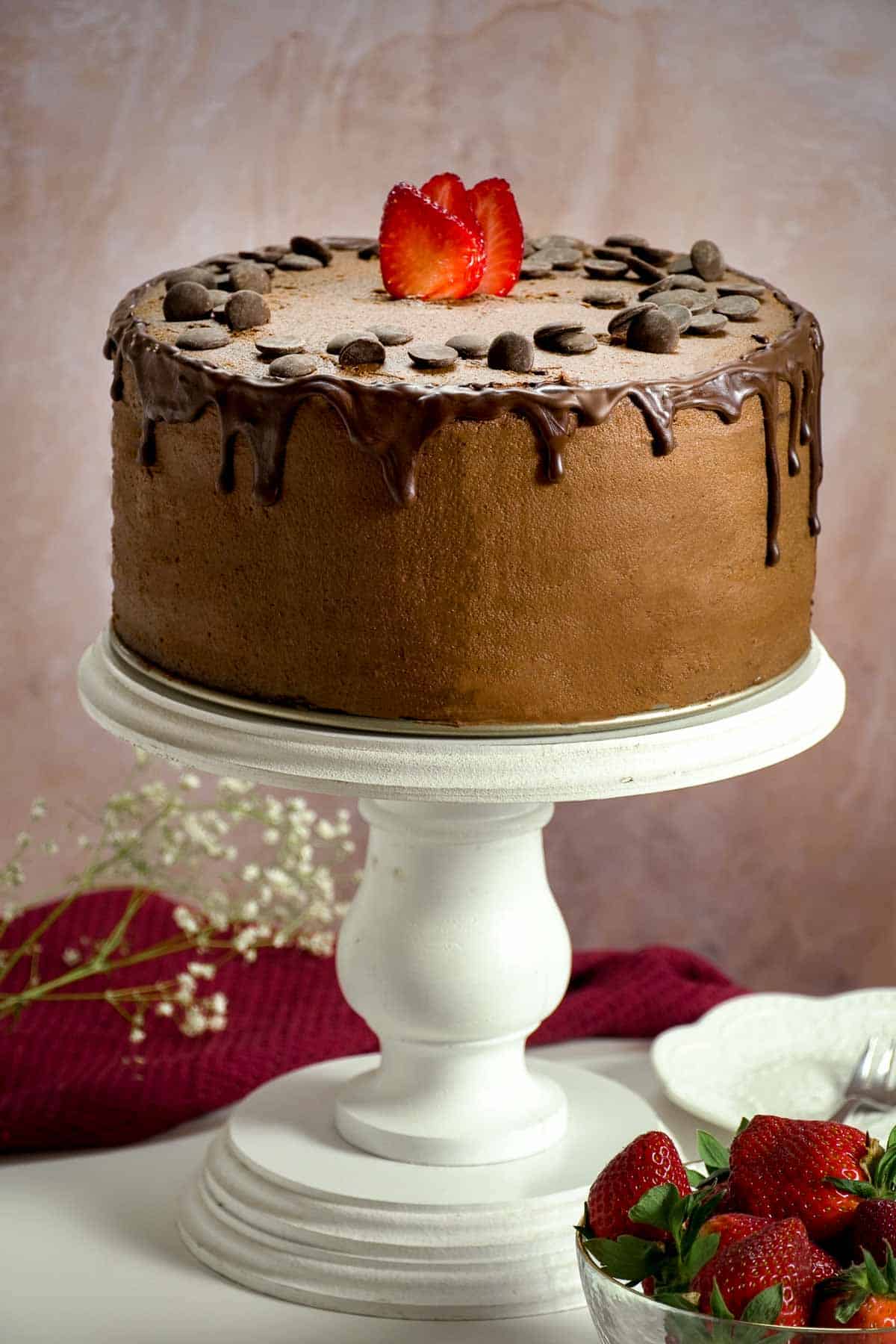 A chocolate cake with ganache drizzling down the side on a tall white cake stand.