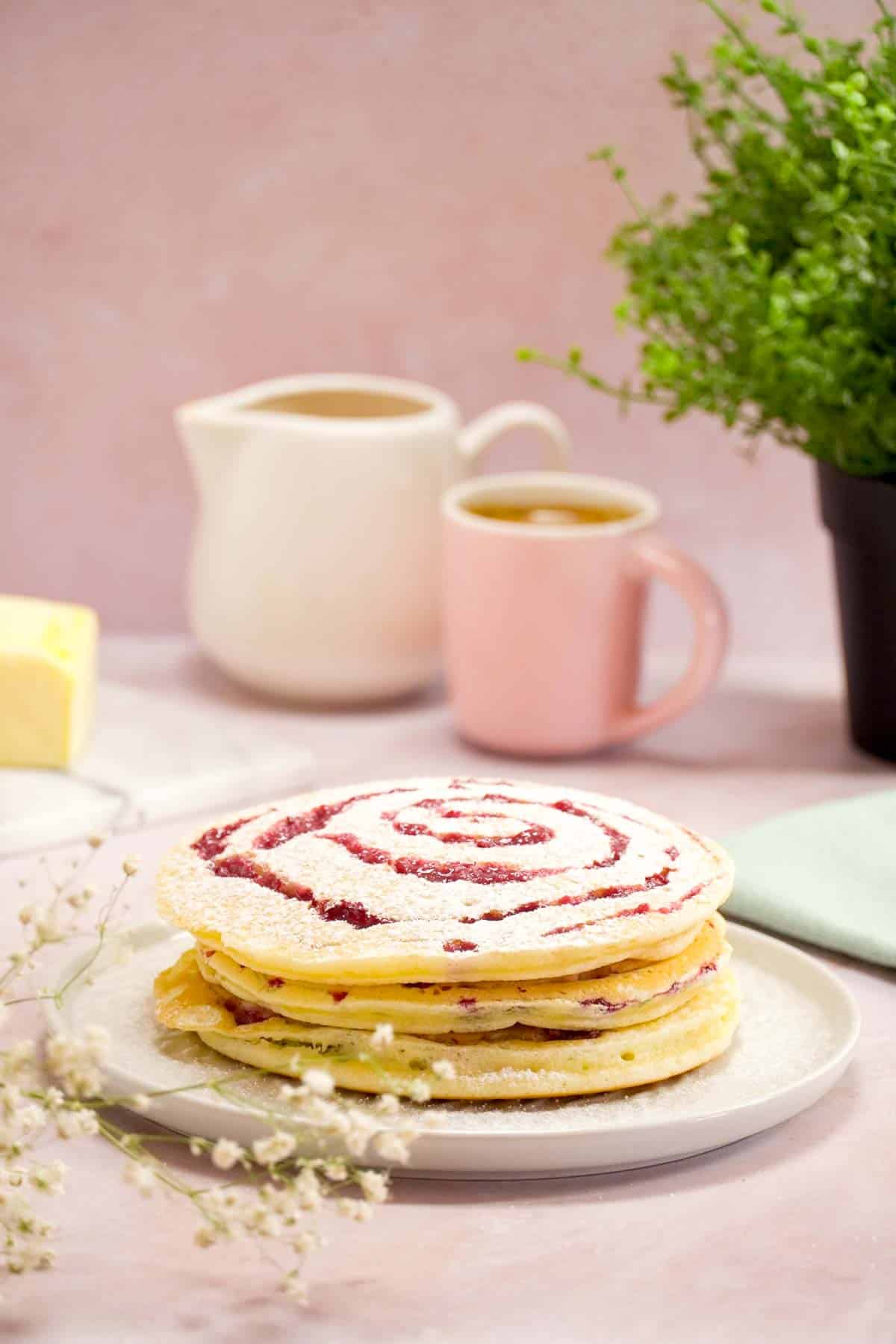 Pancakes with raspberry puree in a swirled pattern stacked on a white plate.
