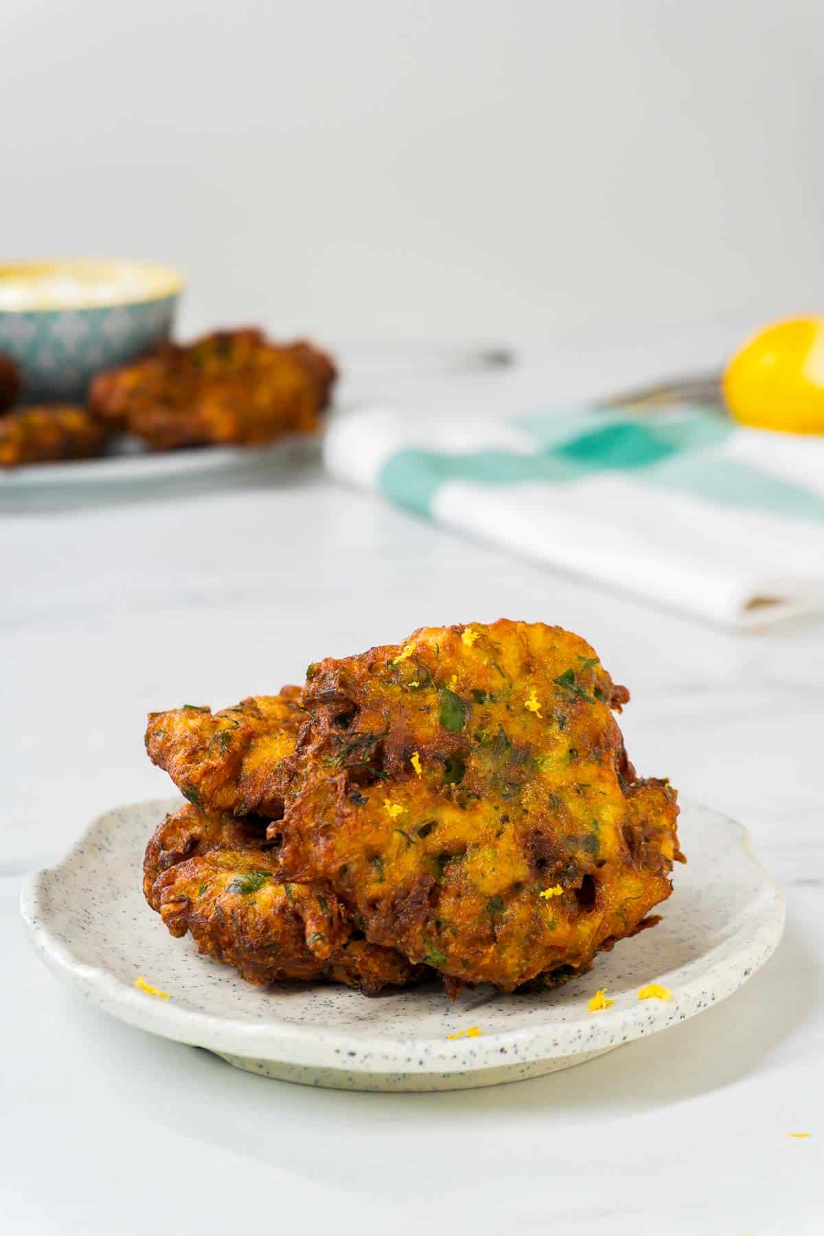 Two mucver pieces on a white dish. There is some lemon zest sprinkled atop the fritters.