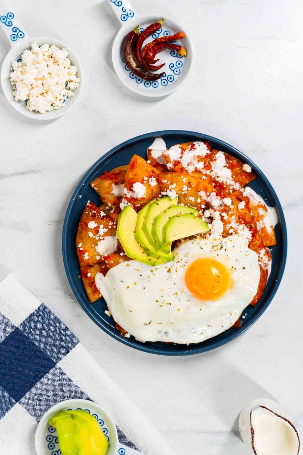 A plate of red chilaquiles, served with avocado, fried egg, Mexican crema, and queso fresco.