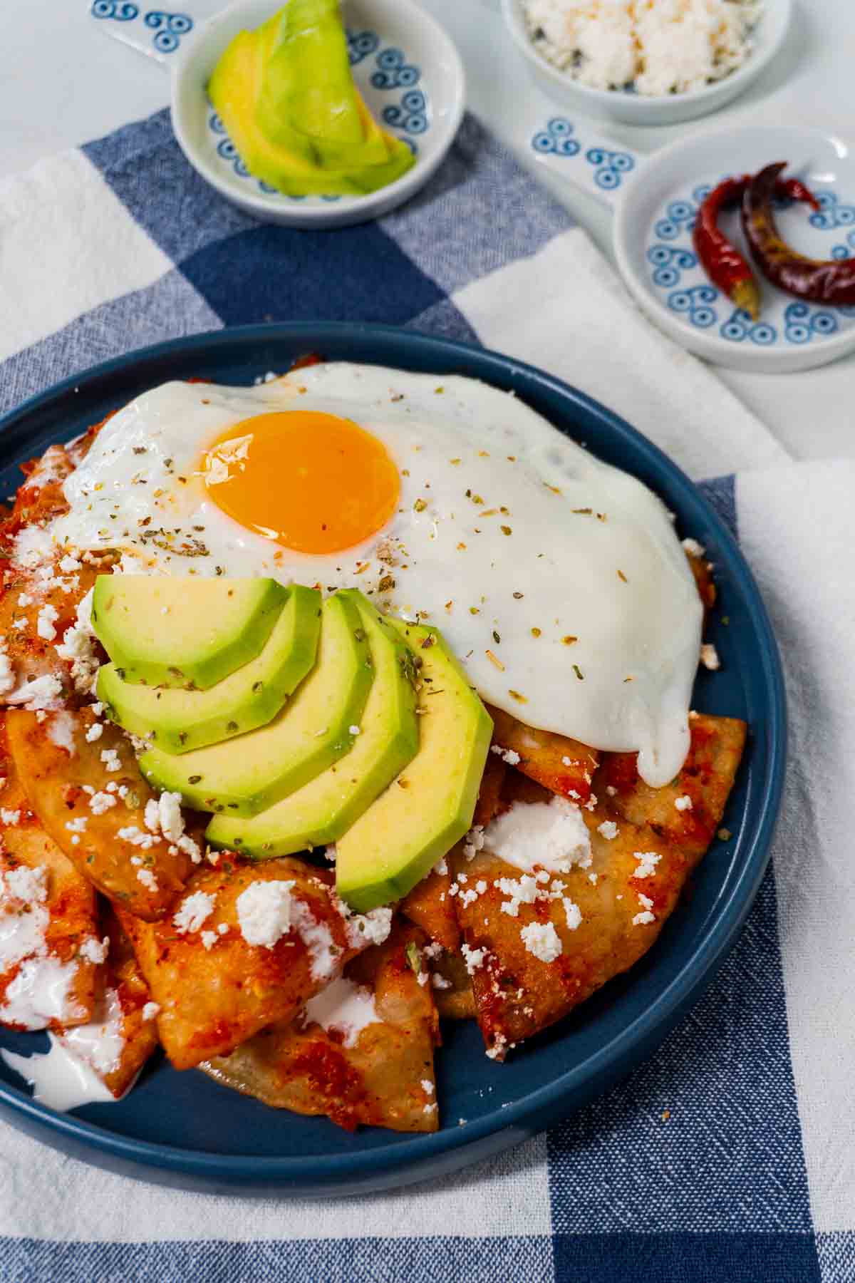 A plateful of Mexican chilaquiles rojos served with a fried egg, avocado slices, crema, and queso fresco.