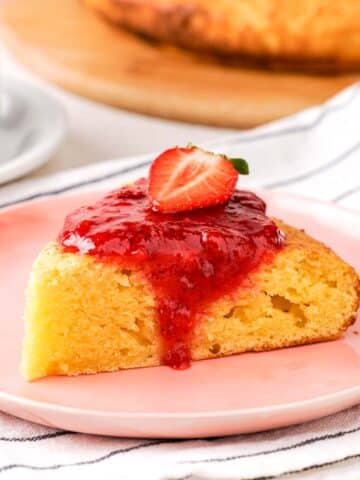 A slice of cottage cheese cheesecake with strawberry sauce on a pink plate.