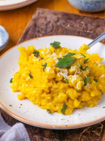 Pumpkin risotto, garnished with sage, on a white plate.