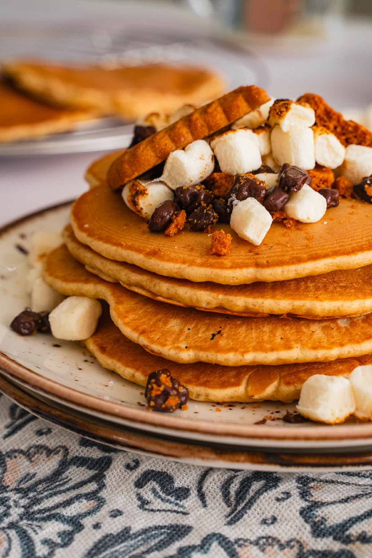 A tall stack of smores pancakes on a white and brown plate.