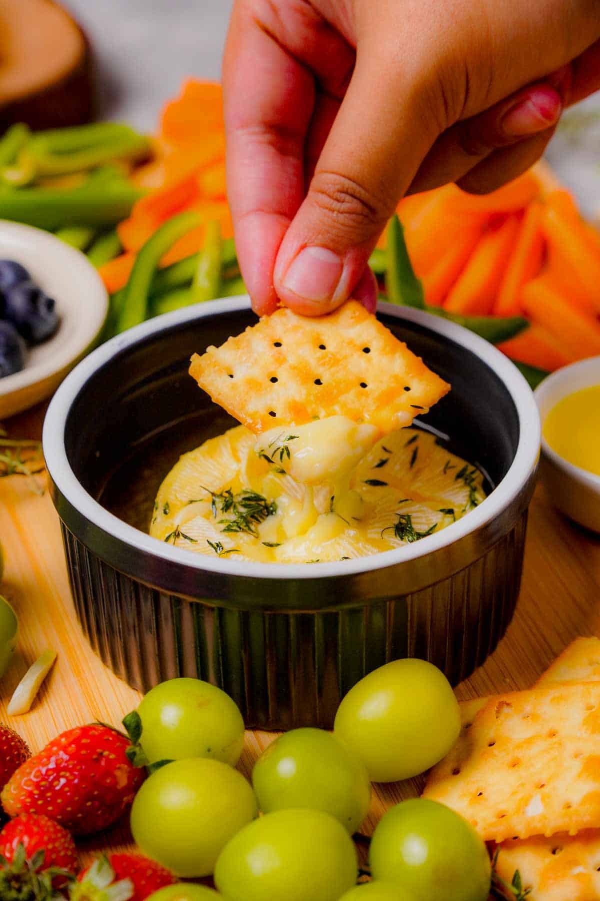 A cracker being dipped into baked brie with garlic and thyme.