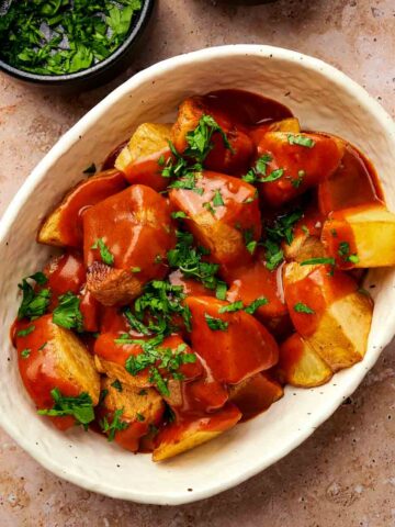 A top down view of a bowl of patatas bravas garnished with parsley.