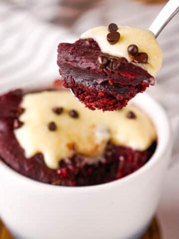 A spoonful of red velvet mug cake topped with cream cheese frosting.