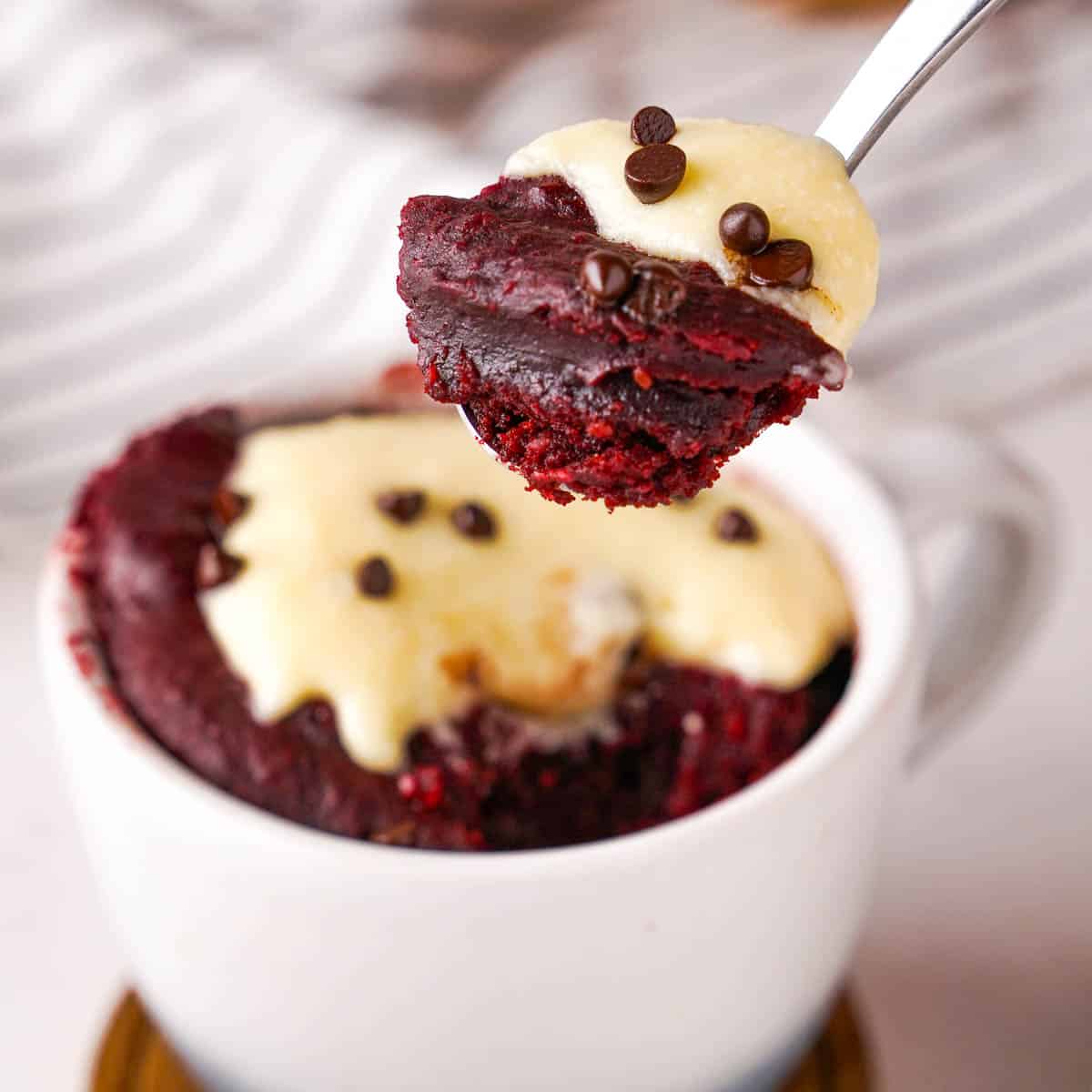 A spoonful of red velvet cake being taken out of a mug.