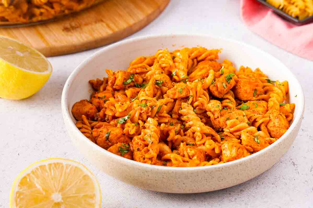 A white bowl containing butter chicken pasta with some small garnishes.