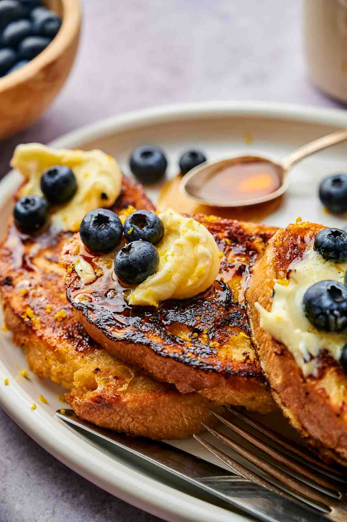 Lemon and blueberry mascarpone French toast on a white plate. Some additional blueberries are visible in the background.