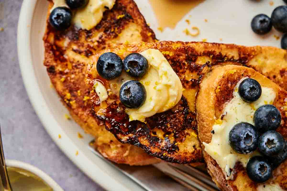 A close-up shot of blueberries and a generous helping of mascarpone cheese on French toast.