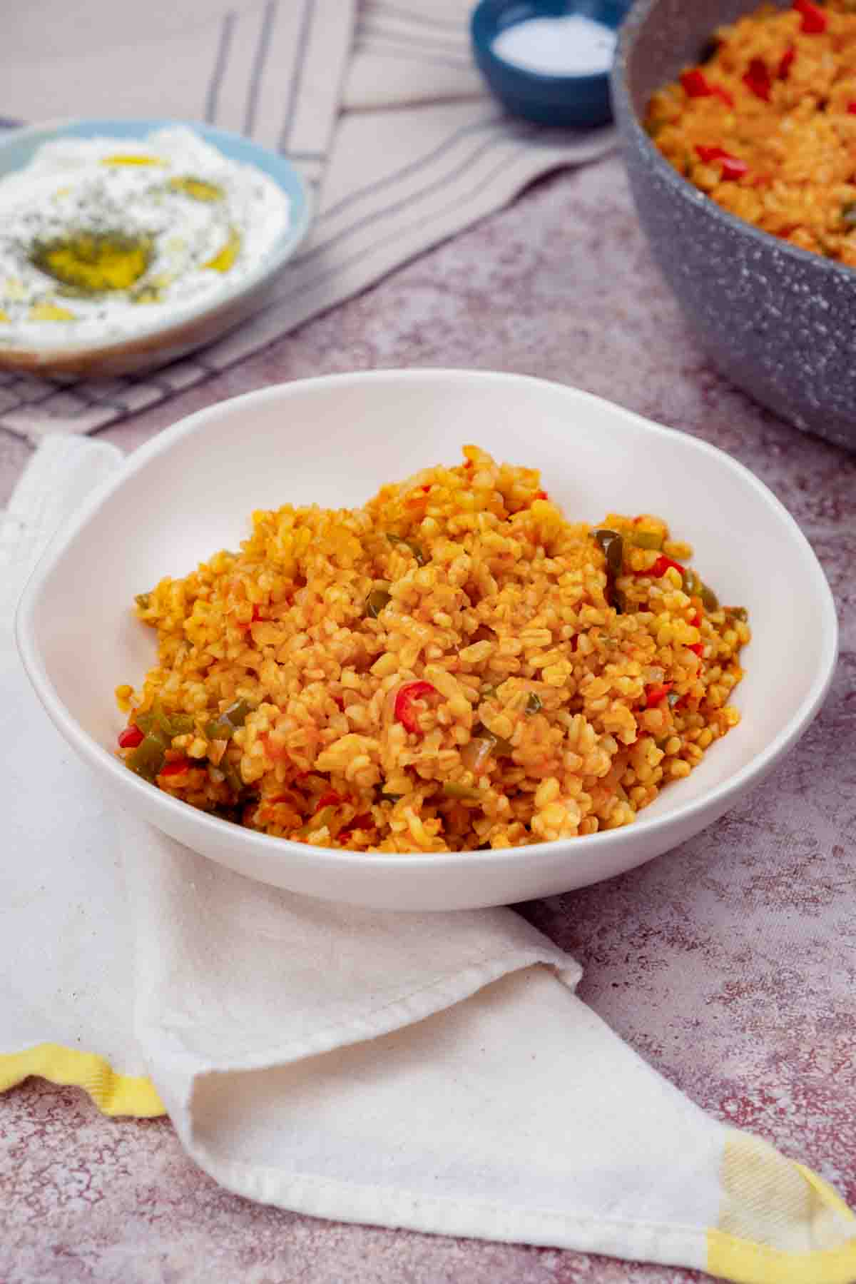 A table setting with a bowl of bulgur cooked with tomatoes and spices.