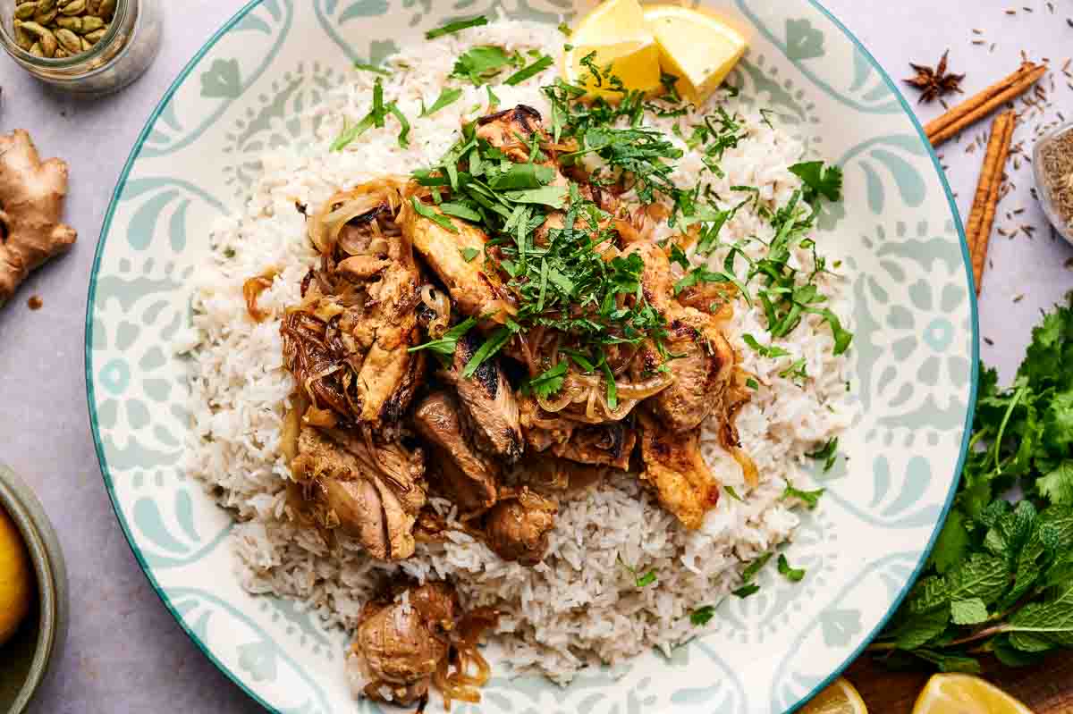 A plate of biryani rice with chicken, garnished with cilantro and two small lemon wedges.