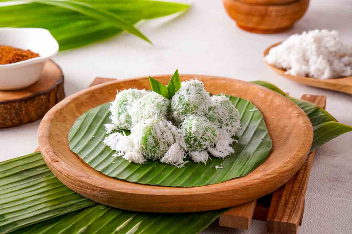 A batch of green Indonesian klepon on a banana leaf on a wooden serving dish.