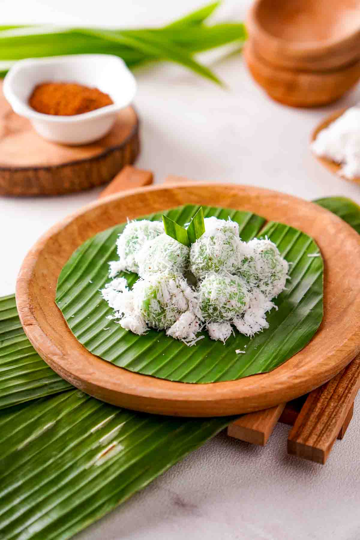 Indonesian klepon on a leaf. Palm sugar, in a white bowl, can be seen in the background.