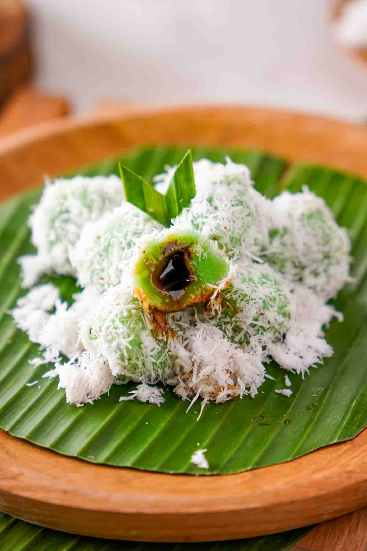 A half-eaten klepon shows the melted palm sugar syrup inside of the green glutinous rice ball.