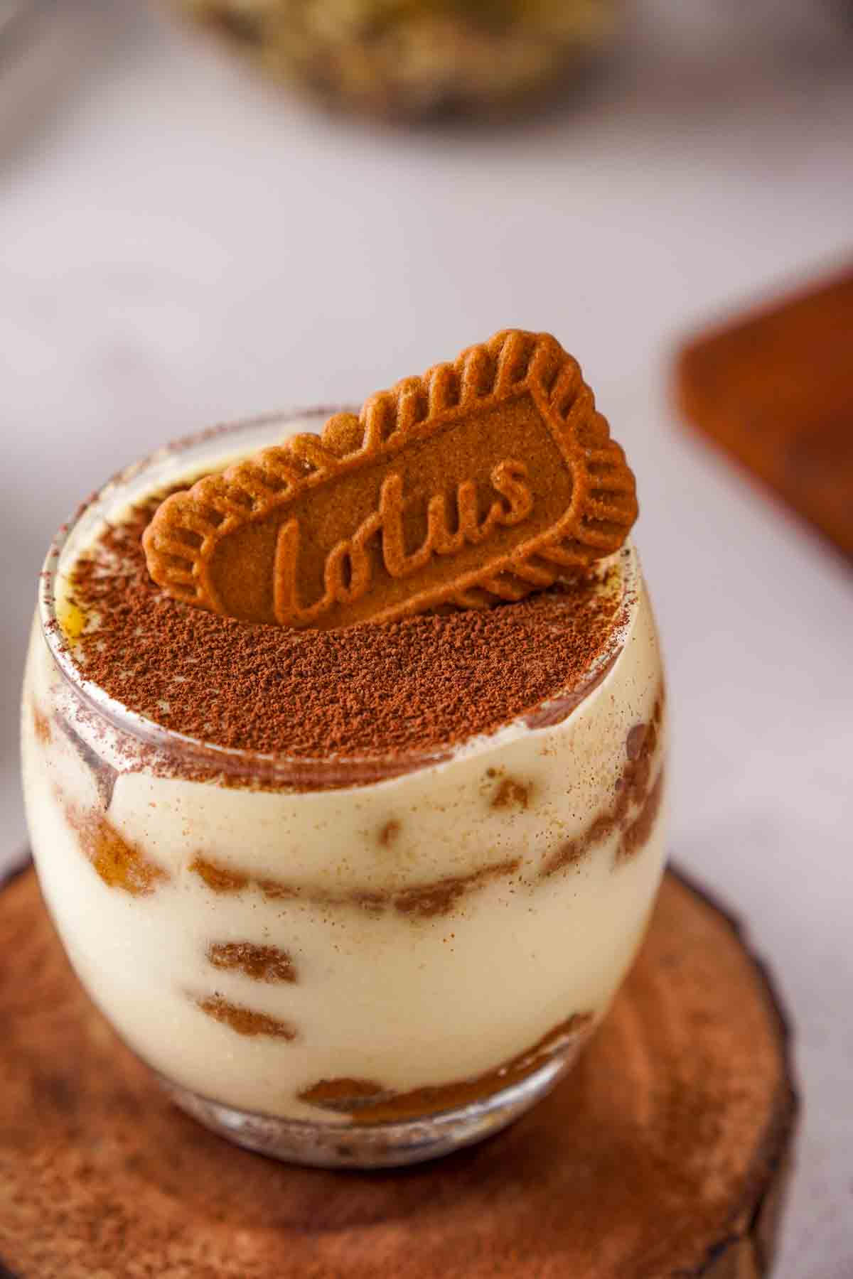 A short tumbler filled with speculoos tiramisu. The tiramisu is topped with cocoa powder and a Lotus Biscoff cookie.