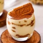 A clear tumbler filled with speculoos tiramisu topped with cocoa powder and a Lotus biscoff cookie.