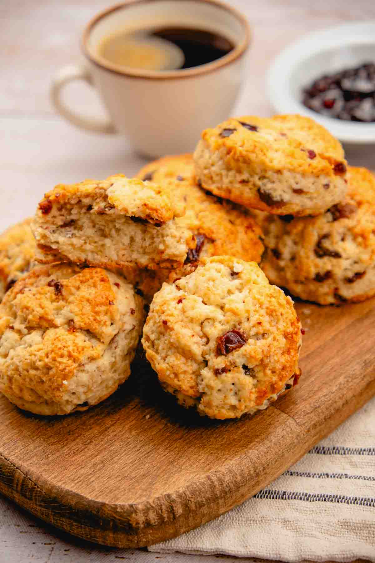 Scones made with chopped and pitted dates served on a wooden platter. A cup of coffee and a bowl of dates are visible in the background.