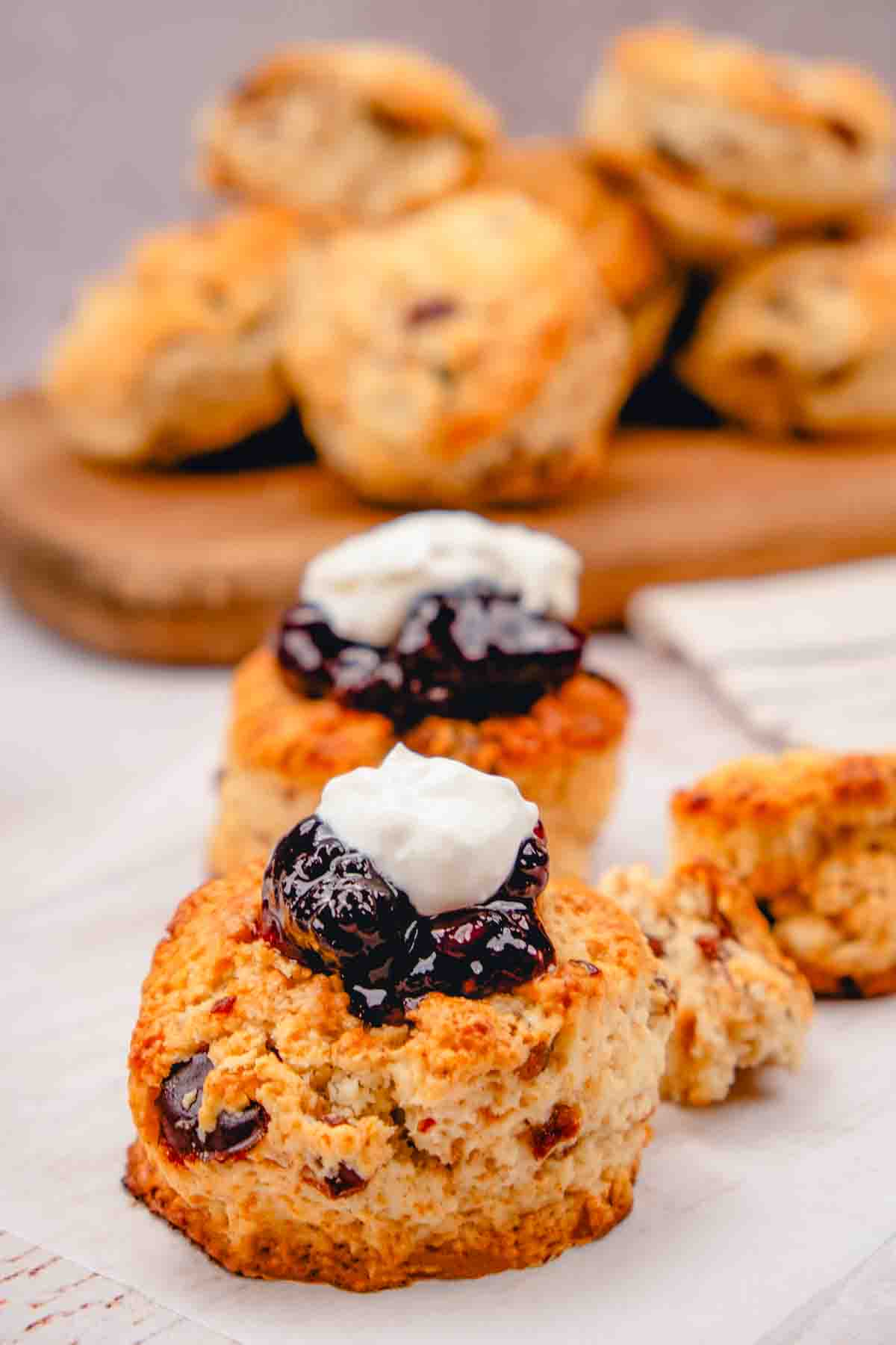 A date scone topped with jam and cream. More scones are visible in the background.