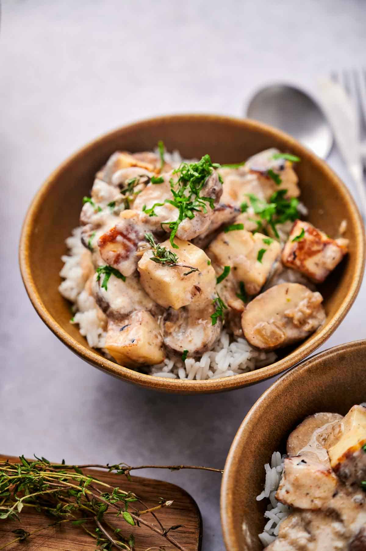 A vegetarian stroganoff made using halloumi cheese, in a brown bowl, served over white rice.