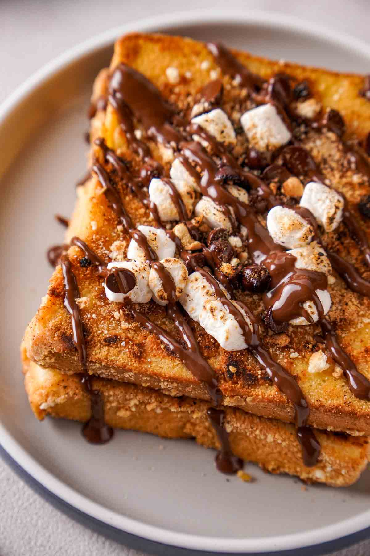 A close-up of French toast, topped with chocolate chips, crushed graham crackers, toasted marshmallows, and melted chocolate.