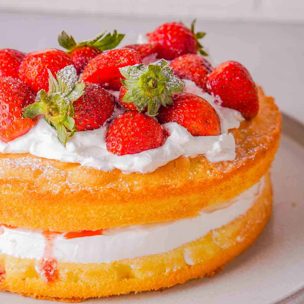 A Victoria Sponge Cake with strawberries on a white platter.