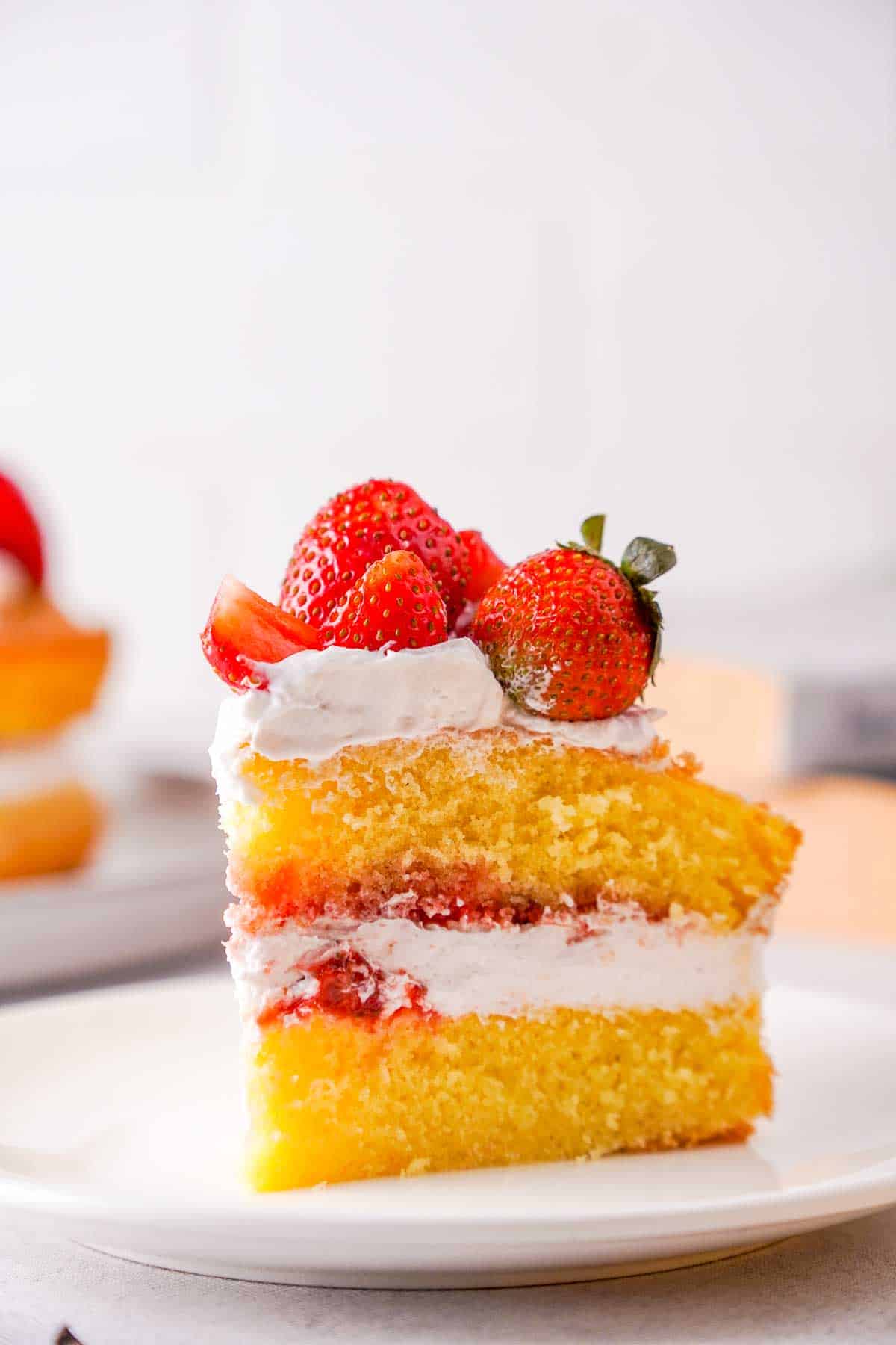 A photo showing the layers of a Victoria Sandwich slice. The strawberry jam, whipped cream, and fresh strawberries are all clearly visible.
