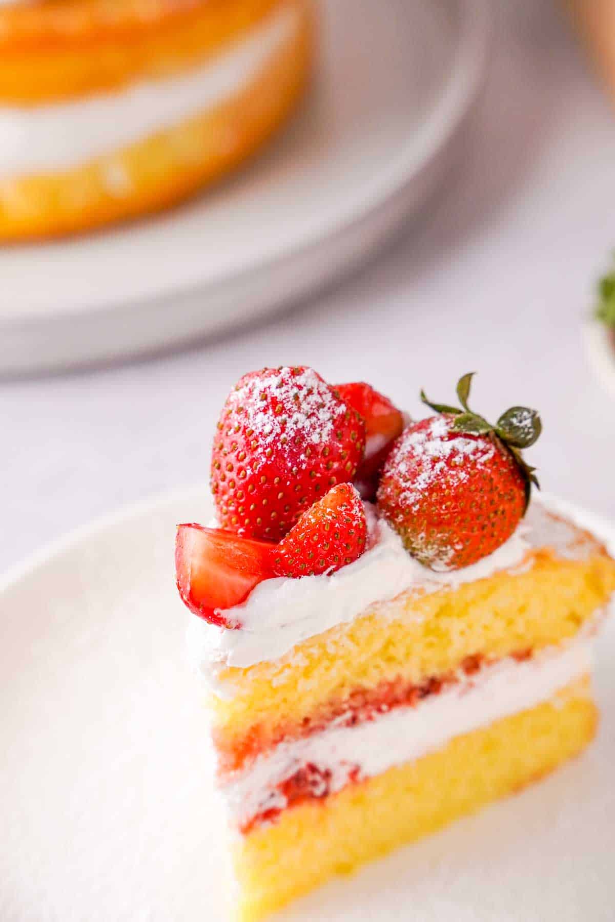 A slice of strawberry Victoria sponge cake on a white plate.