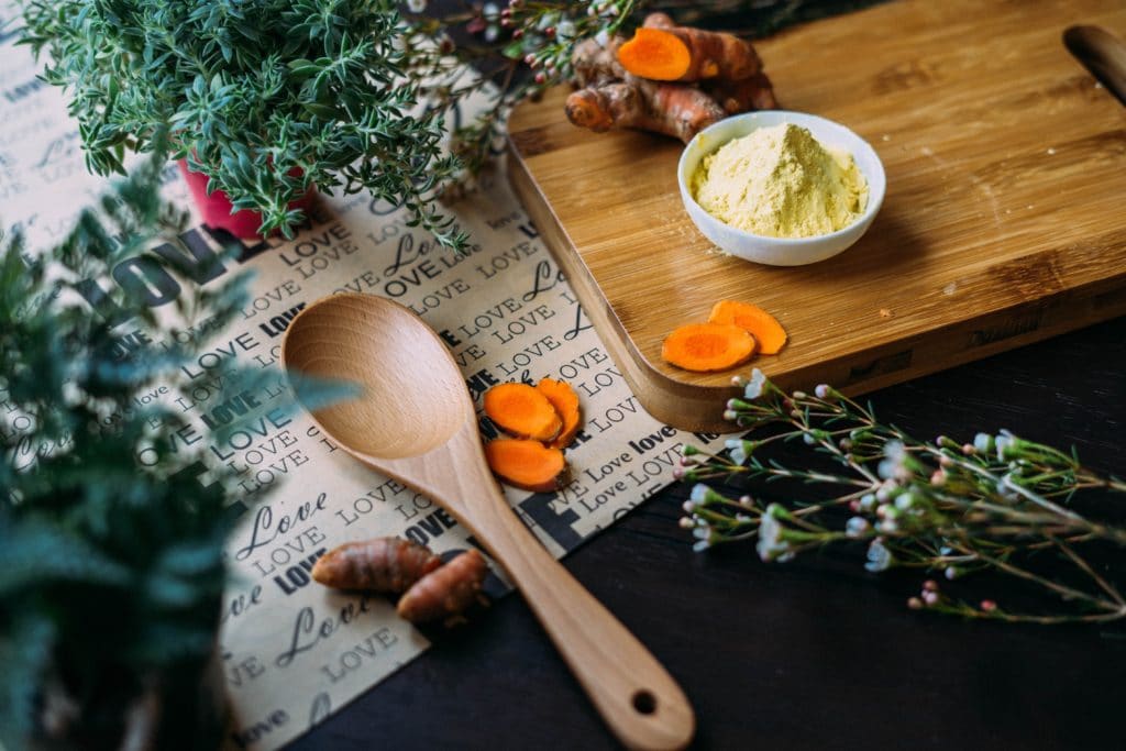 A photo of a wooden spoon, and some sliced sweet potato on a dark wooden board.