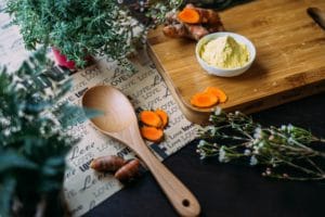 A photo of a wooden spoon, and some chopped carrots on a dark wooden board.