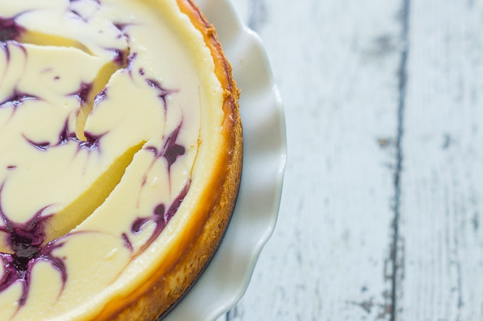 An overhead shot of one half of a Blueberry Swirl Cheesecake on a white cake stand.