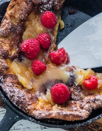 Overhead shot of a cast-iron pan containing a Dutch Baby Pancake, with lemon curd and raspberries spread on top.