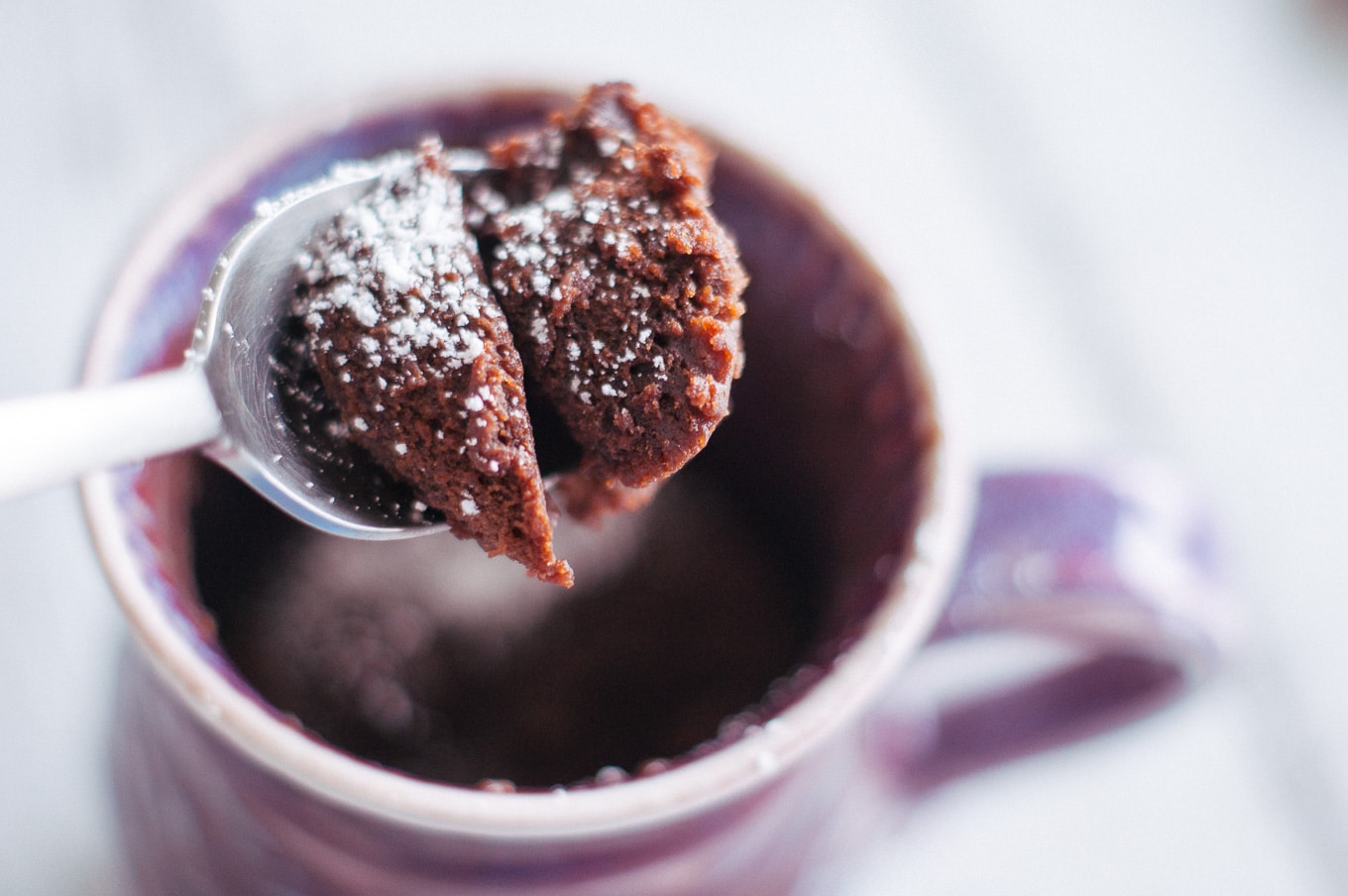 Chocolate mug cake on a spoon with eponymous mug blurred in the background.
