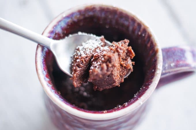 A spoonful of chocolate cake with the mug in the background on white wood.